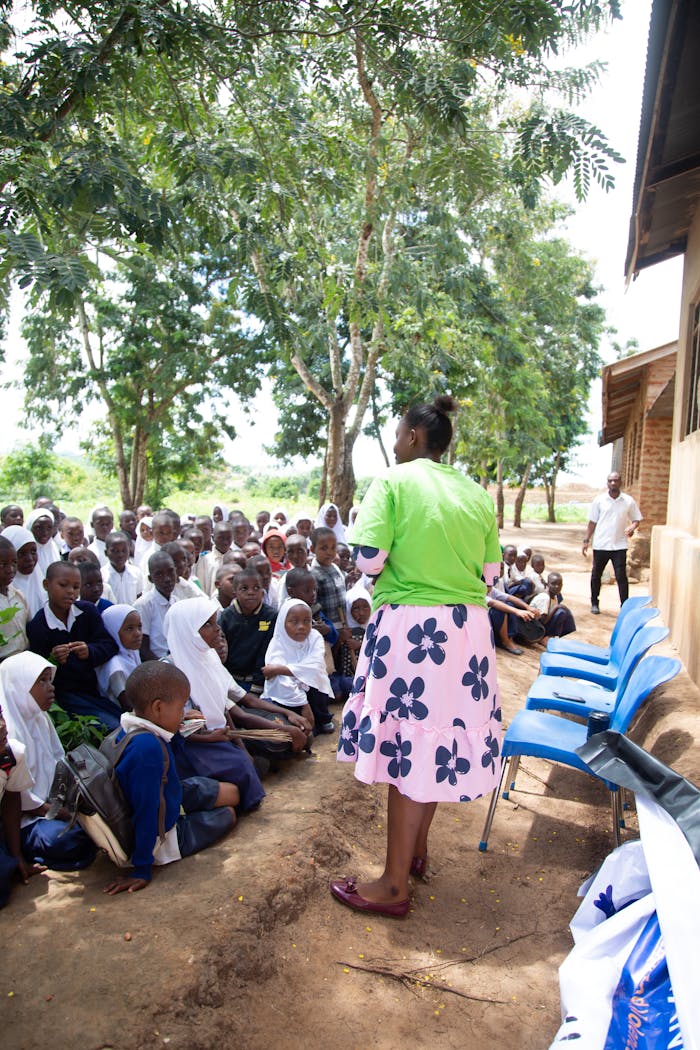 Promouvoir la Santé au Cœur des Communautés : L'Approche de CHECOM Teacher conducts outdoor lesson with attentive children under trees.